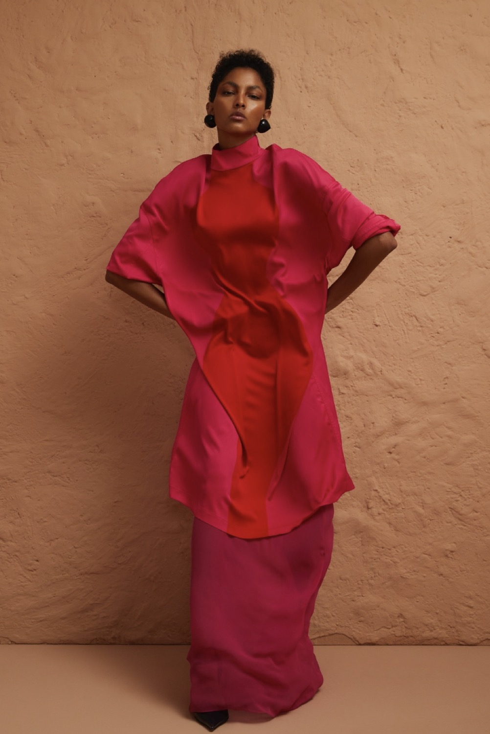 Hair and make-up for a Glamour editorial, model in a red-and-pink dress against a terracotta wall